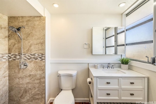 bathroom with a tile shower, vanity, and toilet