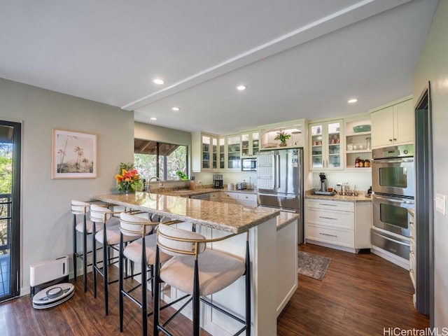 kitchen with white cabinets, kitchen peninsula, light stone countertops, a breakfast bar, and appliances with stainless steel finishes