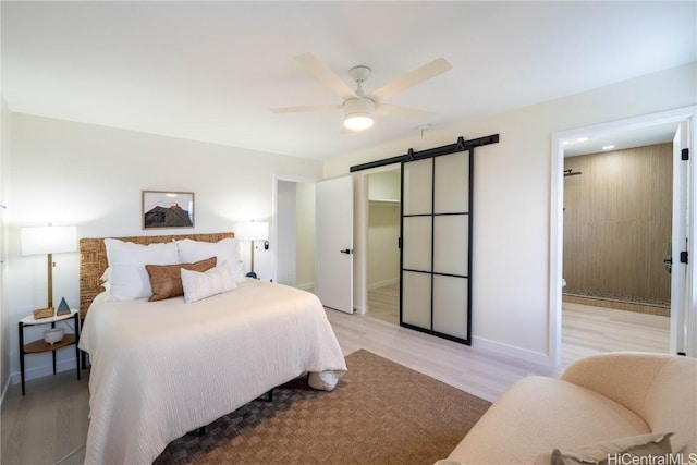 bedroom with a barn door, ceiling fan, and light wood-type flooring