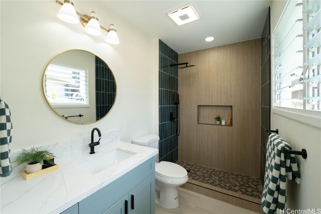 bathroom with toilet, vanity, a healthy amount of sunlight, and tiled shower