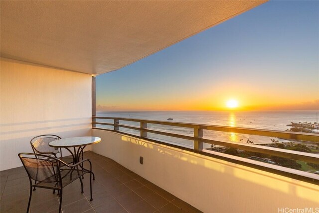 balcony at dusk featuring a water view