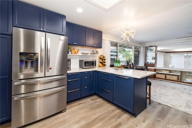 kitchen with stainless steel appliances, blue cabinets, light stone counters, light hardwood / wood-style floors, and kitchen peninsula