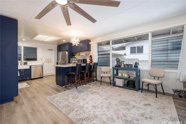 kitchen with blue cabinets, stainless steel appliances, light wood-type flooring, and a kitchen breakfast bar