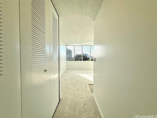 corridor with a textured ceiling and light carpet