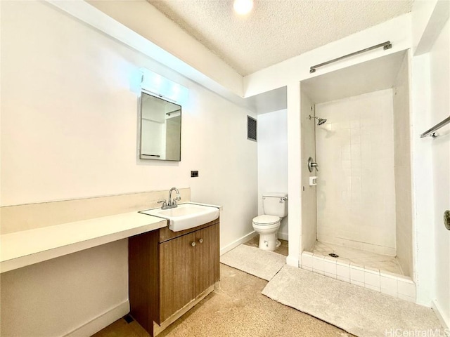 bathroom with a tile shower, vanity, a textured ceiling, and toilet