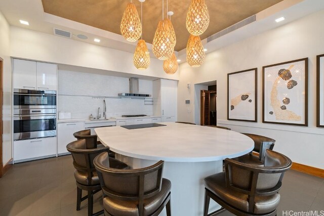 kitchen featuring white cabinetry, tasteful backsplash, decorative light fixtures, a raised ceiling, and wall chimney exhaust hood