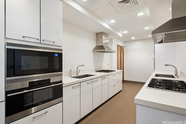 kitchen with ventilation hood, sink, white cabinets, stainless steel appliances, and wall chimney range hood