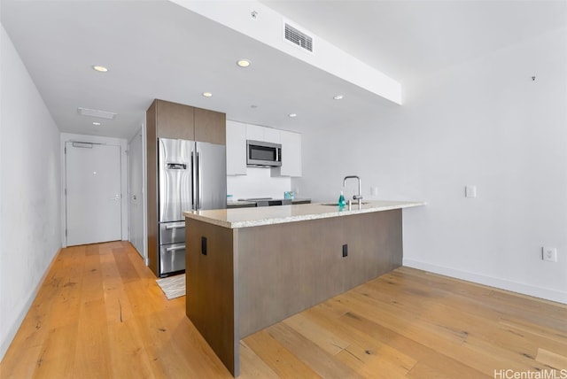 kitchen with white cabinets, appliances with stainless steel finishes, sink, kitchen peninsula, and light hardwood / wood-style flooring