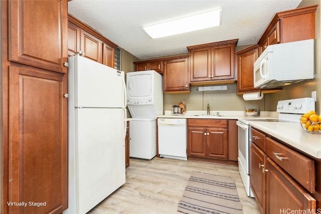 kitchen with white appliances, sink, light hardwood / wood-style flooring, a textured ceiling, and stacked washer / dryer