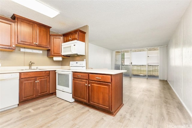 kitchen with white appliances, sink, light wood-type flooring, a textured ceiling, and kitchen peninsula