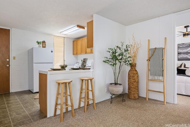 kitchen featuring dark colored carpet, a kitchen breakfast bar, white refrigerator, and a textured ceiling