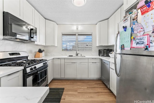 kitchen featuring white cabinets, sink, light wood-type flooring, a textured ceiling, and stainless steel appliances