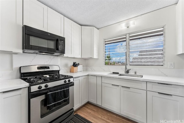 kitchen featuring a textured ceiling, gas stove, sink, light hardwood / wood-style floors, and white cabinetry