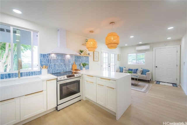 kitchen with hanging light fixtures, white electric stove, premium range hood, kitchen peninsula, and a wall mounted AC