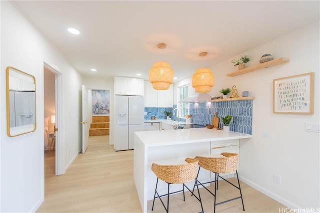 kitchen featuring kitchen peninsula, pendant lighting, white cabinets, white fridge with ice dispenser, and a breakfast bar area