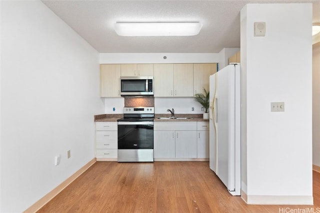 kitchen featuring baseboards, stainless steel appliances, a textured ceiling, light wood-style floors, and a sink