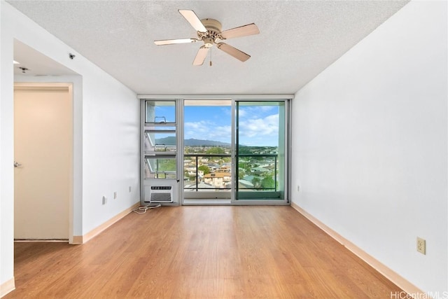 unfurnished room featuring floor to ceiling windows, a wall unit AC, a textured ceiling, wood finished floors, and baseboards