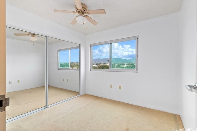 unfurnished bedroom featuring carpet, a textured ceiling, a closet, and ceiling fan