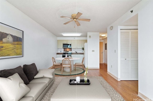 living room with light wood finished floors, baseboards, a ceiling fan, and a textured ceiling