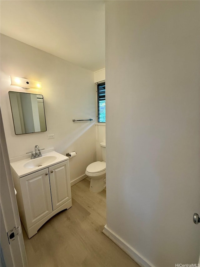 bathroom with baseboards, wood finished floors, vanity, and toilet