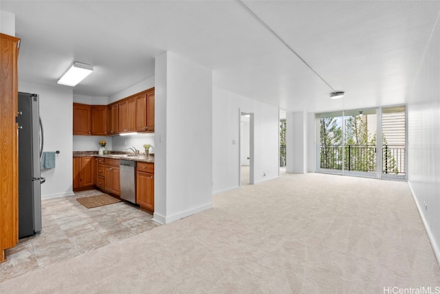 kitchen featuring light colored carpet, appliances with stainless steel finishes, open floor plan, and brown cabinetry