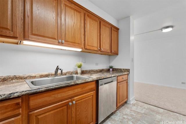 kitchen featuring dark countertops, light colored carpet, brown cabinets, stainless steel dishwasher, and a sink