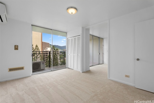 empty room with visible vents, baseboards, a wall of windows, carpet flooring, and a wall mounted AC