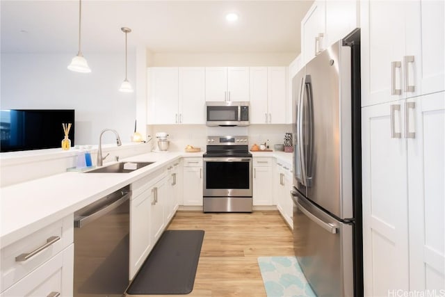 kitchen featuring pendant lighting, stainless steel appliances, light hardwood / wood-style floors, white cabinetry, and sink