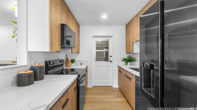 kitchen with black appliances, decorative backsplash, light wood-type flooring, and light stone countertops