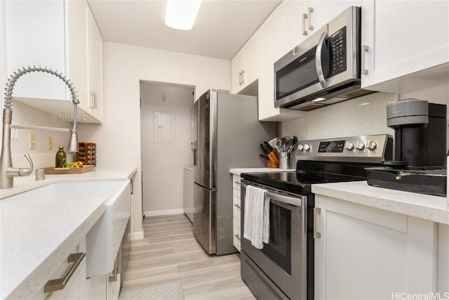 kitchen with light stone countertops, white cabinets, light hardwood / wood-style floors, and appliances with stainless steel finishes