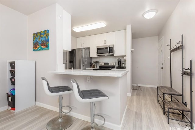 kitchen with kitchen peninsula, appliances with stainless steel finishes, light hardwood / wood-style floors, a kitchen bar, and white cabinetry