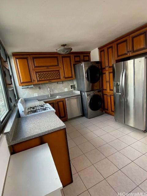 kitchen with appliances with stainless steel finishes, light tile patterned floors, sink, and stacked washer and dryer