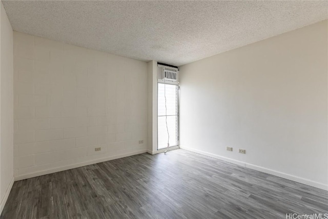 spare room featuring dark wood-type flooring, a wall unit AC, and a textured ceiling