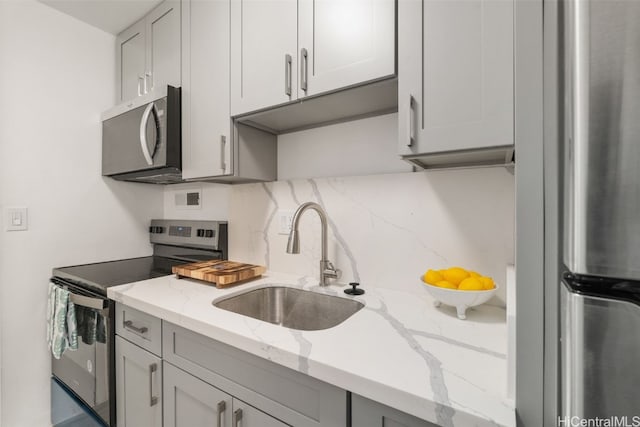 kitchen with gray cabinetry, light stone countertops, sink, and appliances with stainless steel finishes