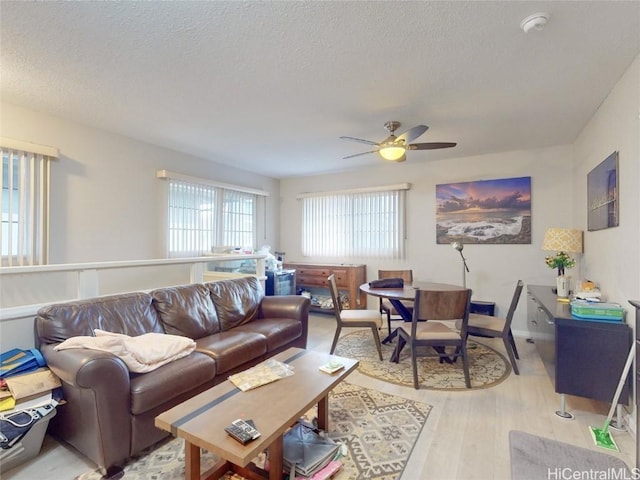 living room with ceiling fan, light wood-type flooring, and a textured ceiling