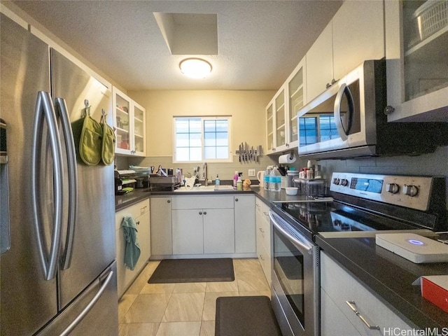 kitchen with sink, light tile patterned floors, a textured ceiling, white cabinetry, and stainless steel appliances