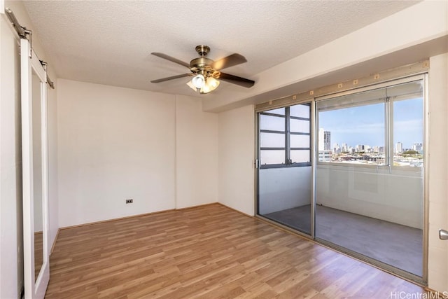 unfurnished bedroom with ceiling fan, a barn door, hardwood / wood-style floors, and a textured ceiling