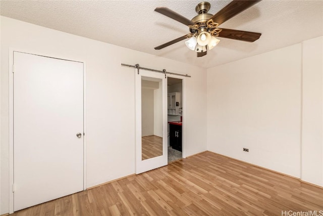 unfurnished bedroom with light wood-type flooring, a textured ceiling, ceiling fan, and a barn door