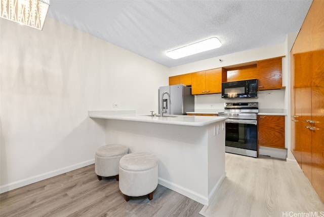 kitchen featuring sink, a kitchen breakfast bar, stainless steel appliances, a textured ceiling, and light hardwood / wood-style flooring