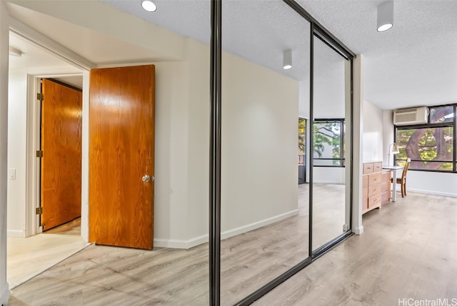 corridor with a wall mounted air conditioner, a textured ceiling, and light wood-type flooring