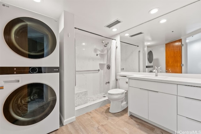 bathroom featuring walk in shower, stacked washer / drying machine, toilet, vanity, and hardwood / wood-style flooring