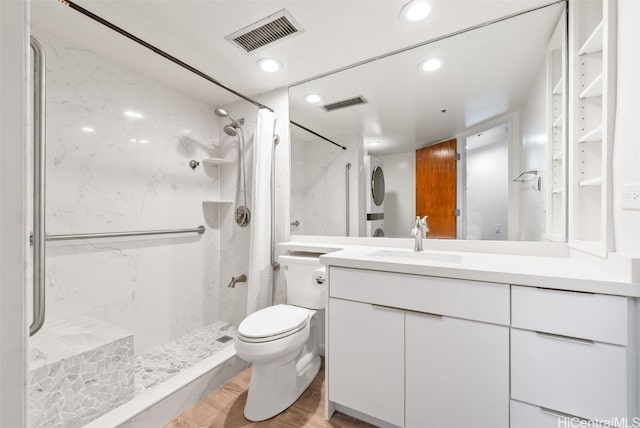 bathroom with hardwood / wood-style flooring, tiled shower, vanity, and toilet