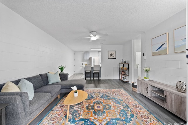 living room with dark wood-type flooring, ceiling fan, and a textured ceiling