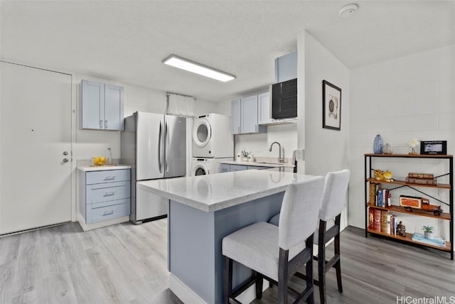 kitchen featuring gray cabinets, stacked washer / dryer, sink, stainless steel fridge, and a textured ceiling