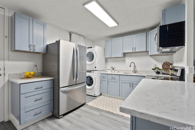 kitchen featuring stacked washer / dryer, sink, stainless steel appliances, a textured ceiling, and light hardwood / wood-style flooring