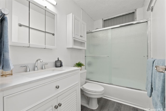 full bathroom featuring hardwood / wood-style floors, bath / shower combo with glass door, vanity, a textured ceiling, and toilet