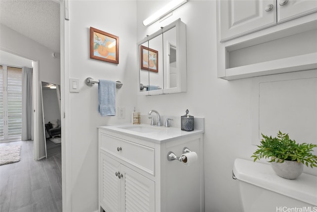 bathroom featuring vanity, toilet, wood-type flooring, and a textured ceiling