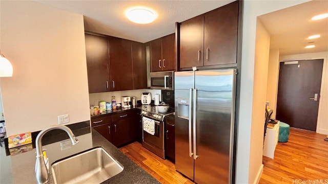 kitchen with dark brown cabinetry, sink, light hardwood / wood-style flooring, and appliances with stainless steel finishes