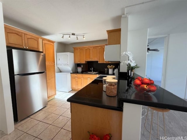 kitchen with backsplash, kitchen peninsula, a kitchen bar, stacked washing maching and dryer, and stainless steel fridge