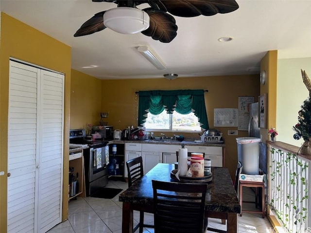 kitchen with stainless steel electric stove, sink, white cabinets, and light tile patterned floors